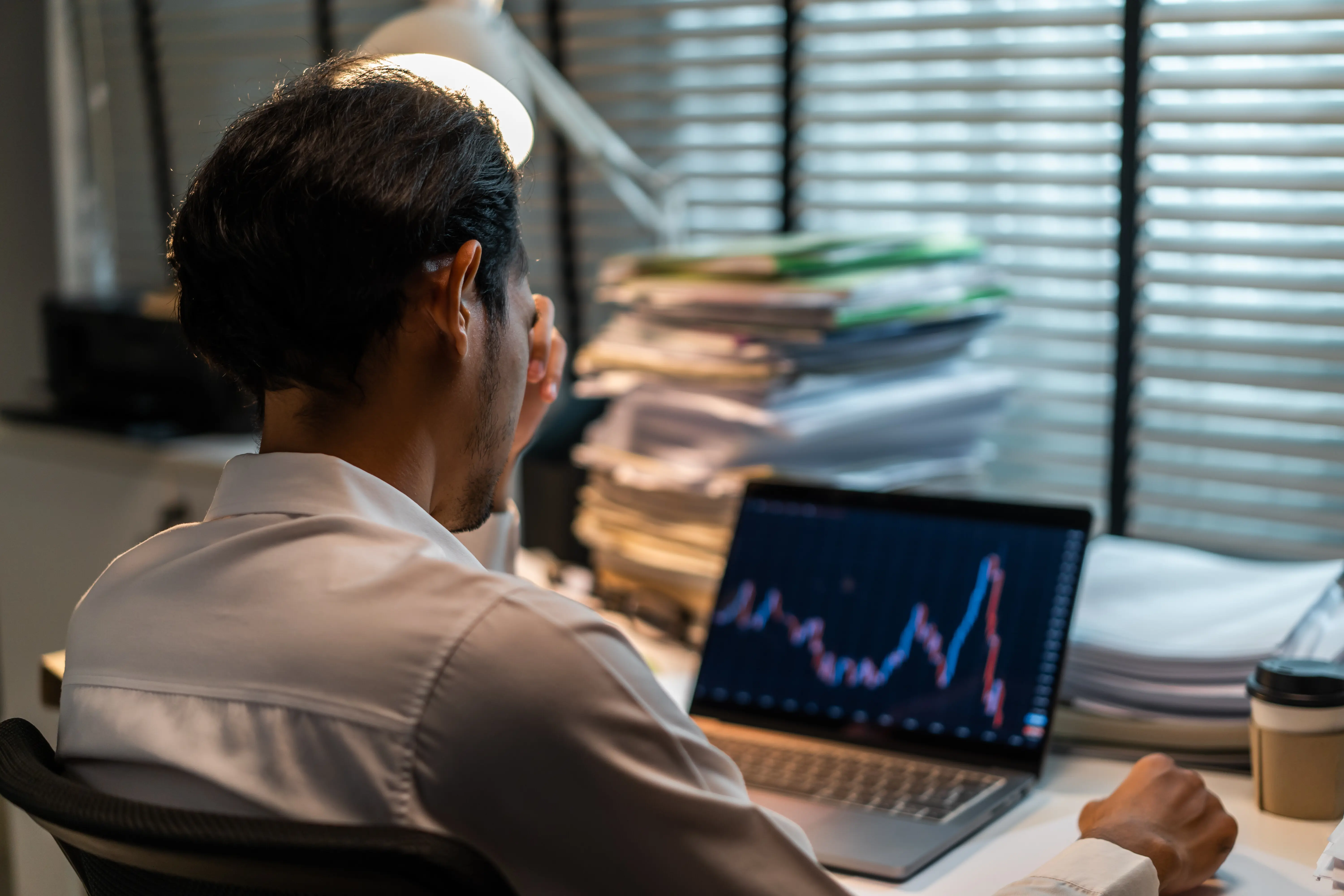 Ein asiatischer, männlicher Broker/Trader und junger angestellter Geschäftsmann analysiert Aktienmarkt-Investitionen und Diagramme, arbeitet am Laptop und überprüft dabei Finanzplanung, Management und Analysen, spät in der Nacht im Büro.